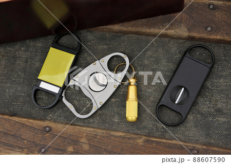 Flatlay Assortment of Cigar Cutters on Rustic Wood Table Beside Cigar Box 88607590