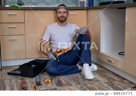 Handsome young caucasian repairman sitting on kitchen floor Handsome young caucasian repairman sitting on kitchen floor 88610775