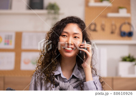 Phone conversation. Confident Asian woman sit on couch talk speak communicate by telephone from home holding device at ear. Phone conversation. Confident Asian woman sit on couch talk speak communicate by telephone from home holding device at ear. 88610926