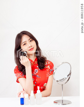 a young asian woman in traditional cheongsam qipao dress looks at mirror and does skin care isolated on white background. 88611958