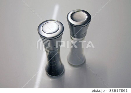 Salt and pepper glass and iron grinders on a white desk 88617861