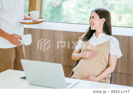 テレワークする妊婦と飲み物を持ってくる男性 88621247