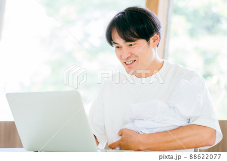 赤ちゃんを抱きながら仕事する男性 88622077