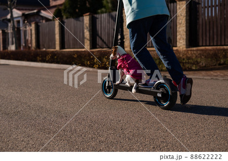 A woman rides an electric scooter in a cottage village with a dog Jack Russell Terrier.  88622222