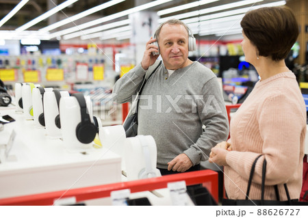 Man trying on headphones while shopping with his wife in electronic store Man trying on headphones while shopping with his wife in electronic store 88626727