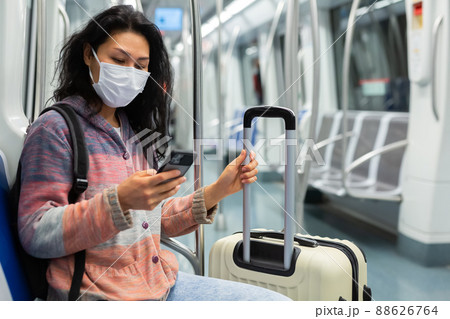 Woman in protective mask with suitcase sitting in subway car and using smartphone 88626764