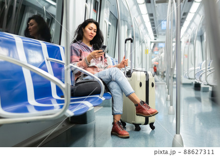 Woman with suitcase sitting in subway car and using her smartphone 88627311