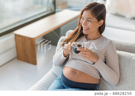 Asian pregnant woman drinking coffee cup at home. Pregnancy foods and drinks to avoid Asian pregnant woman drinking coffee cup at home. Pregnancy foods and drinks to avoid 88628250