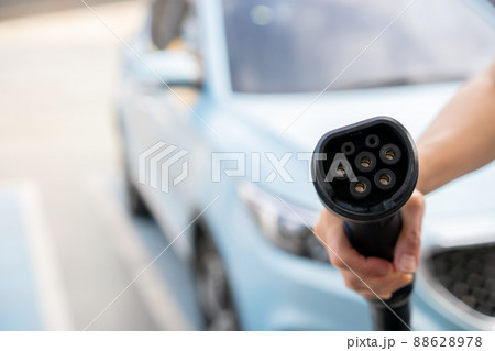 Unrecognizable Asian woman holding AC type 1 EV charging connector at EV charging station, woman preparing an EV - electric vehicle charging connector for recharge a vehicle. Unrecognizable Asian woman holding AC type 1 EV charging connector at EV charging station, woman preparing an EV - electric vehicle charging connector for recharge a vehicle. 88628978