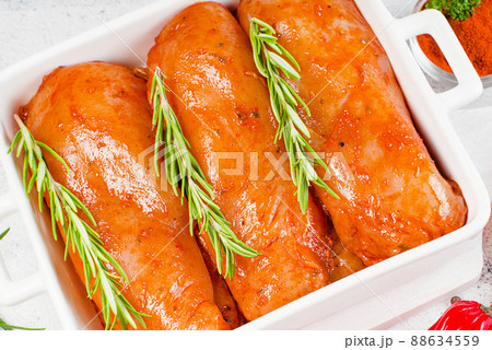 Marinated chicken fillet in red sauce in a plate for roasting in the oven on a light background. Raw marinated chicken fillet with fresh rosemary. 88634559