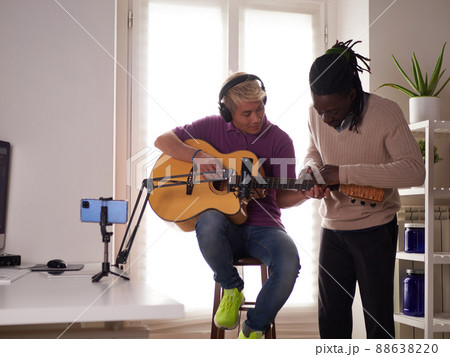 A personal afroamerican tutor explains to his asian student how to play studied chord correctly. Musical education at home 88638220