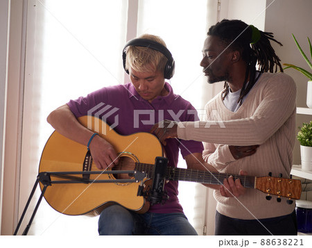 A personal afroamerican tutor explains to his asian student how to play studied chord correctly. Musical education at home 88638221