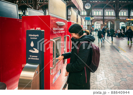 Smiling student girl in winter clothes pays for train fare in red vending machines in the main hall of the Copenhagen Central railway Station. Denmark Smiling student girl in winter clothes pays for train fare in red vending machines in the main hall of the Copenhagen Central railway Station. Denmark 88640944