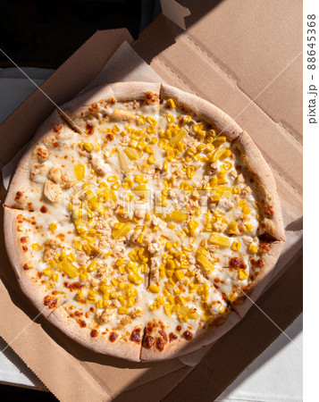 Tasty pizza with pineapple corn mozzarella cheese and white sauce in cardboard box on a table in daylight harsh shadows. Tasty pizza with pineapple corn mozzarella cheese and white sauce in cardboard box on a table in daylight harsh shadows. 88645368