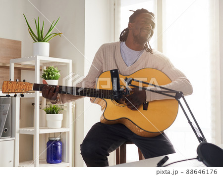 Young man is singing and playing guitar while making an audio recording at home 88646176