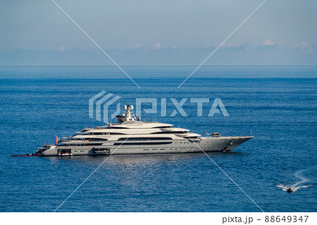 The huge mega yacht is moored in sea off the coast of the azur coastline at sunny day, the chrome plated handrail, sun reflection on glossy board of the motor boat The huge mega yacht is moored in sea off the coast of the azur coastline at sunny day, the chrome plated handrail, sun reflection on glossy board of the motor boat 88649347
