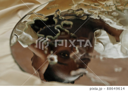 Close-up of reflection of young African woman looking through drops in mirror Close-up of reflection of young African woman looking through drops in mirror 88649614