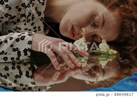 Young woman lying with her eyes closed and touching the flower lying on wet mirror 88649617