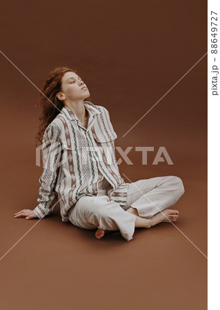 Portrait of young woman with red hair sitting in relaxed pose against the brown background 88649727