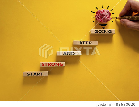 Start strong and keep going symbol. Concept words 'Start strong and keep going' on wooden blocks on a beautiful yellow background. Businessman hand. Business, motivational and start strong concept. 88650620