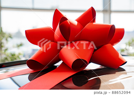 a red gift bow on the roof of a new black car in the car dealership. a red gift bow on the roof of a new black car in the car dealership. 88652094