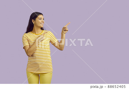 Young smiling woman pointing fingers at content copy space on pastel purple background. 88652405