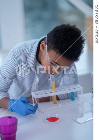 A dark-haired boy in a lab coat looking busy while doing chemical experiment 88653301