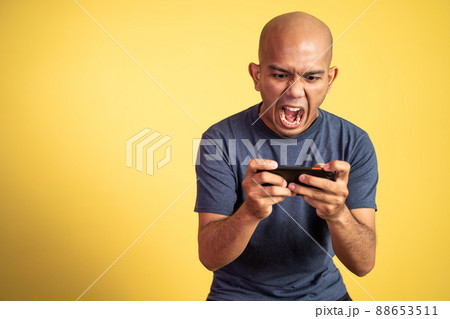 Bald asian man shouting while playing game using smartphone 88653511