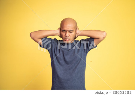 bald man with uncomfortable expression with hands covering ears 88653583