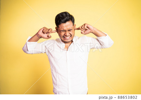 asian young man with uncomfortable expression with fingers covering ears asian young man with uncomfortable expression with fingers covering ears 88653802