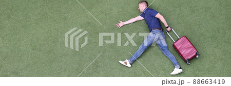 Young man with suitcase walking on green grass top view 88663419