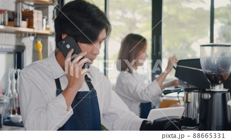 barista man coffee maker receive phone call and record pre order to computer in coffee cafe shop 88665331