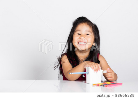 Little cute kid girl 3-4 years old smile using pencil sharpener while doing homework in studio shot isolated Little cute kid girl 3-4 years old smile using pencil sharpener while doing homework in studio shot isolated 88666539