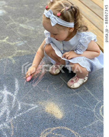 Little girl drawing with colorful chalks on playground 88667345