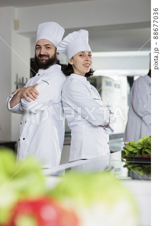 Skilled cooks wearing cooking uniforms while posing back to back in restaurant kitchen space. Multiethnic gastronomy experts standing in arms crossed while smiling at camera. Skilled cooks wearing cooking uniforms while posing back to back in restaurant kitchen space. Multiethnic gastronomy experts standing in arms crossed while smiling at camera. 88677036