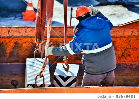 Professional slinger in construction helmet at factory unloads cargo. Boot training. Worker in warm Professional slinger in construction helmet at factory unloads cargo. Boot training. Worker in warm 88679481