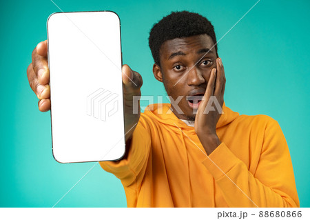 Smiling casual black man pointing at blank white cell phone screen in studio Smiling casual black man pointing at blank white cell phone screen in studio 88680866