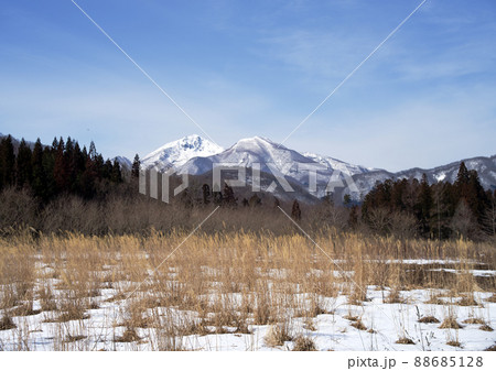 早春の草原と残雪の磐梯山。雪の残る草原と冠雪の磐梯山が青空に綺麗だ 