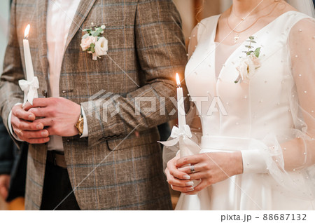 The bride and groom hold shining candles during the ceremony in the church. Hands of newlyweds with candles in the church. Church religious details. Traditions The bride and groom hold shining candles during the ceremony in the church. Hands of newlyweds with candles in the church. Church religious details. Traditions 88687132