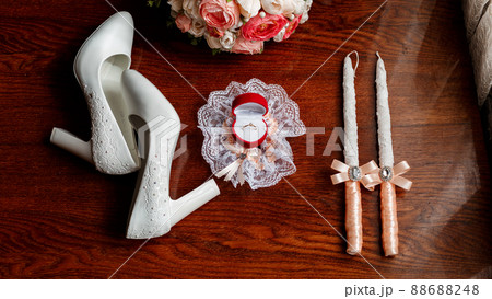 Morning of the bride. Bridal bouquet. Wedding candles in the church. Wedding rings in a red box. White shoes of the bride. Garter on the leg of the bride. Bridal accessories Morning of the bride. Bridal bouquet. Wedding candles in the church. Wedding rings in a red box. White shoes of the bride. Garter on the leg of the bride. Bridal accessories 88688248