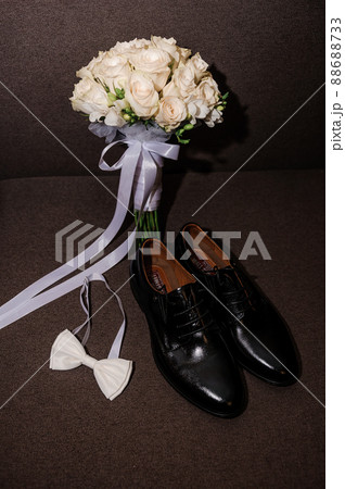 White bow tie, black classic shoes and bridal bouquet with white roses on a brown background 88688733