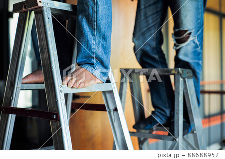 Selective focus on the aluminum ladder with defocused feet of workers working on it Selective focus on the aluminum ladder with defocused feet of workers working on it 88688952