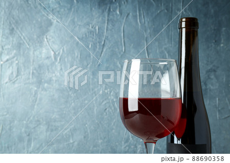 Bottle and glass of red wine against blue textured background 88690358