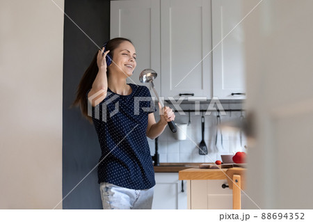 Woman in headphones holds ladle like mike singing feels carefree Woman in headphones holds ladle like mike singing feels carefree 88694352