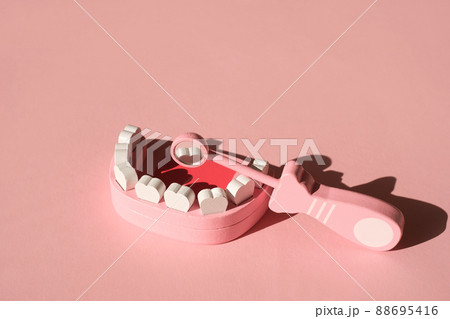 Model of a human jaw with a dentist's mirror, in which the tooth is reflected from the inside of the oral cavity. Medical dental instruments for examination on a pink studio background with Copy space Model of a human jaw with a dentist's mirror, in which the tooth is reflected from the inside of the oral cavity. Medical dental instruments for examination on a pink studio background with Copy space 88695416