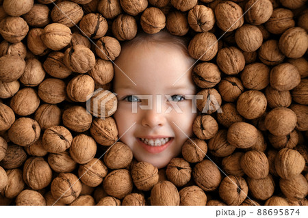 The face of a funny smiling girl is surrounded by a large pile of whole unpeeled walnuts. Allergy to nuts in children The face of a funny smiling girl is surrounded by a large pile of whole unpeeled walnuts. Allergy to nuts in children 88695874