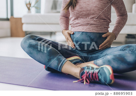 Activewear for pregnancy. Maternity clothes woman wearing full panel yoga leggings for bodyweight workout at home on floor mat Activewear for pregnancy. Maternity clothes woman wearing full panel yoga leggings for bodyweight workout at home on floor mat 88695903