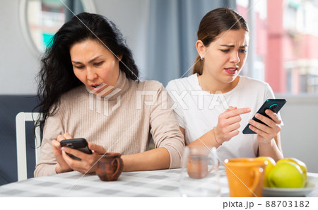 Two women typing text on the smartphone while sitting at table at home Two women typing text on the smartphone while sitting at table at home 88703182