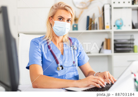 Female doctor in in protective medical mask working on laptop Female doctor in in protective medical mask working on laptop 88703184