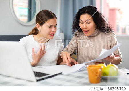 Two women with financial documents near laptop sitting at table at home 88703569